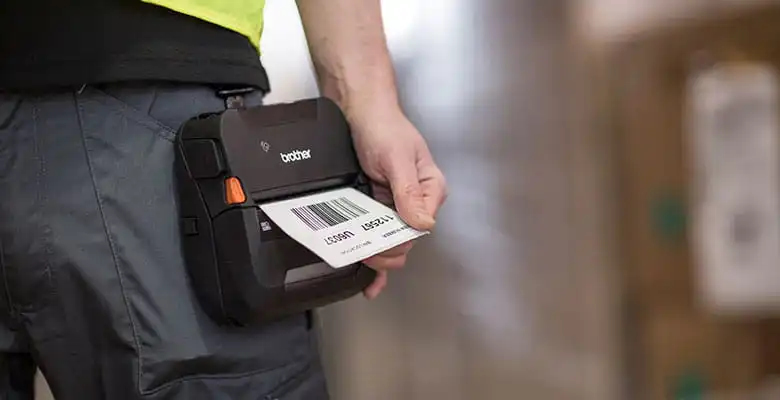 Iemand gebruikt een Brother-etikettenprinter die aan zijn riem is bevestigd om snel een barcodelabel af te drukken.