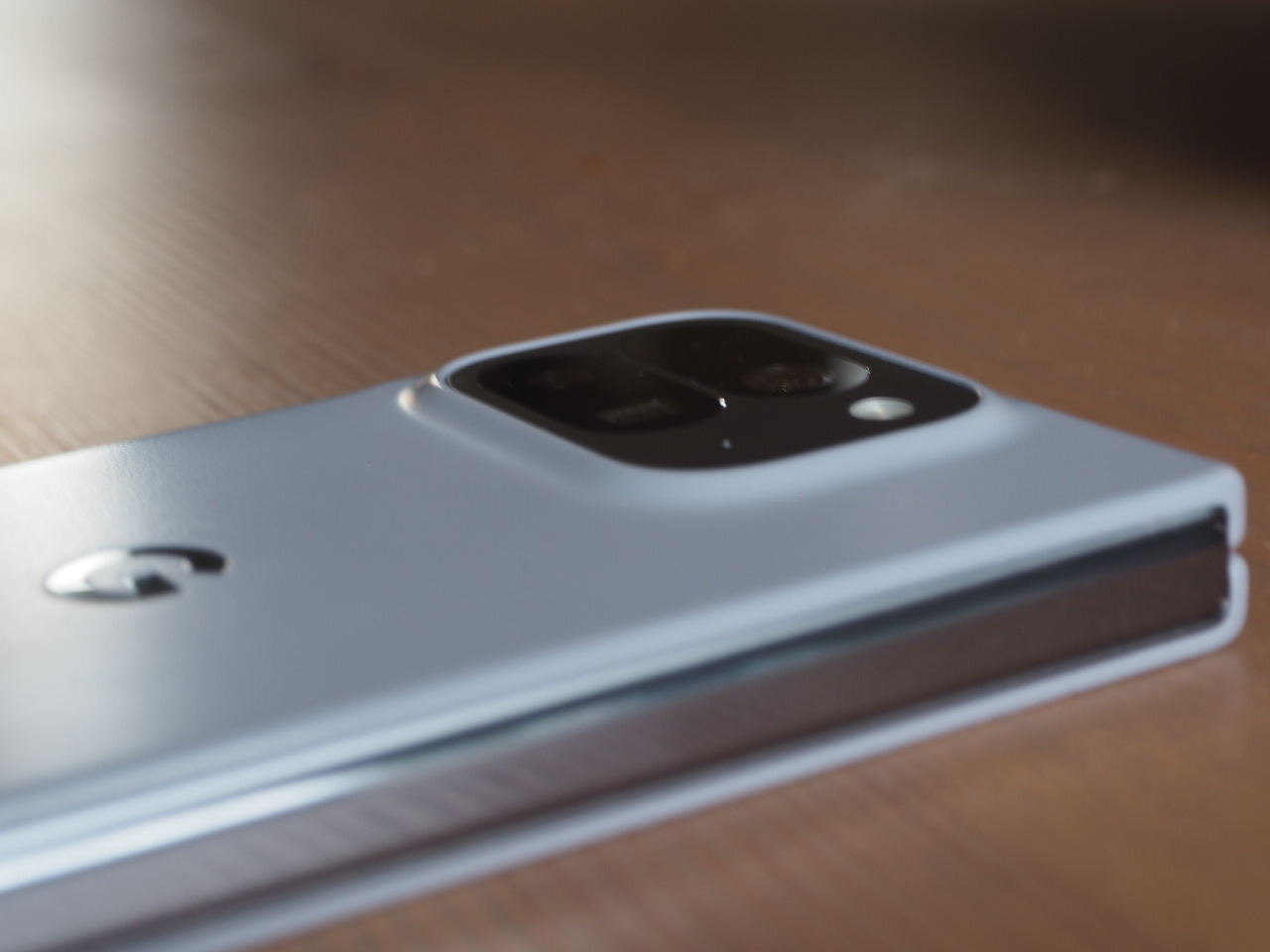 Een close-up van een opgevouwen smartphone met een zichtbare cameramodule, liggend op een houten oppervlak.